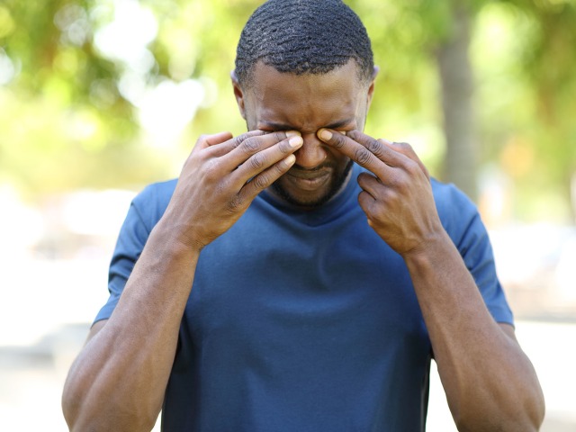Man scratching itchy eyes in a park